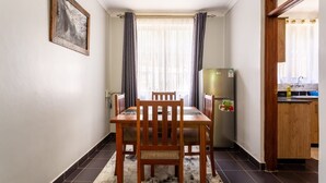 A small dining area with a table and chairs, a refrigerator, and a kitchen counter. - Tanga Suites (Nairobi)