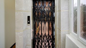 An elevator with a black metal gate, a control panel, and a window with a view of greenery outside. - Deluxe Super Collection O Kollur Prime (Hyderabad)