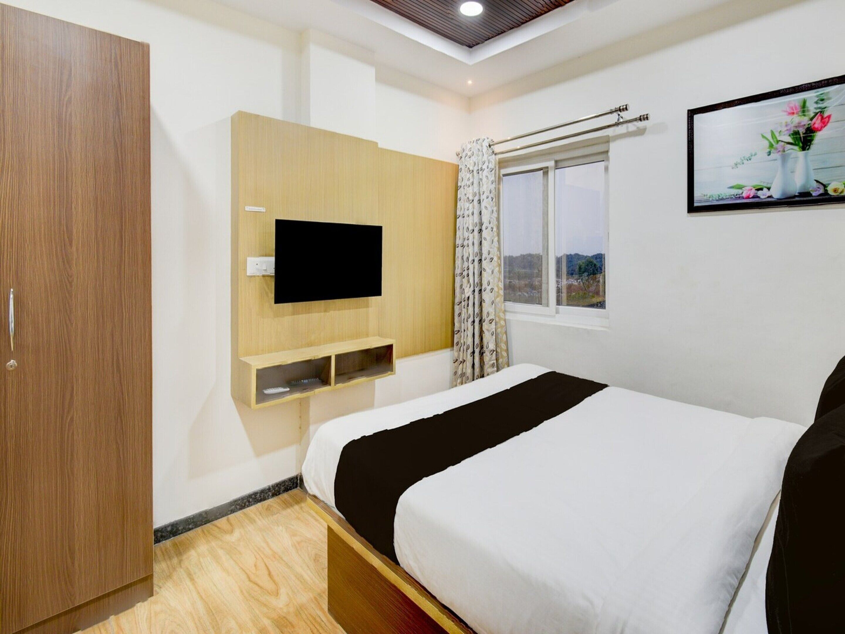 Ein Hotelzimmer mit Bett, Wandfernseher, Fenster mit Vorhängen und einem Holzschrank.