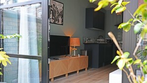 A modern living room with a TV, wooden console, lamp, and kitchen area visible through an open door. - Eldon Terrace - Luxury 1 Bedroom Property (York)