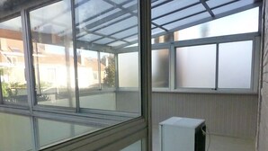 Ein Zimmer mit großen Fenstern, einem kleinen weißen Heizgerät und Blick auf Gebäude.
