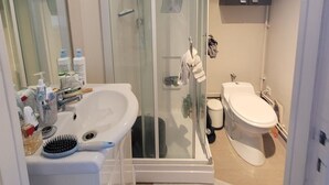 Ein Badezimmer mit Duschkabine, Waschbecken mit Pflegeprodukten, Toilette und Schrank.