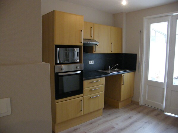 A kitchen with wooden cabinets, a microwave, an oven, a sink, and a door leading to a balcony.