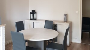 Ein Essbereich mit einem runden Tisch, sechs Stühlen, einer modernen Pendelleuchte, einer Kaffeemaschine und einem Kühlschrank.