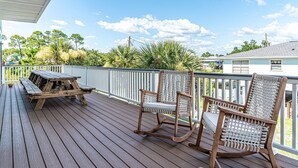 A wooden deck with a picnic table and two rocking chairs. - Retreat in Gulf Shores| Luxury Pool• Tanning Shelf • Putting Green •Sleeps 14 (Gulf Shores)