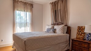 A bedroom with a bed, curtains, a nightstand, and a decorative item. - Retreat in Gulf Shores| Luxury Pool• Tanning Shelf • Putting Green •Sleeps 14 (Gulf Shores)