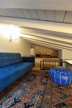 A modern living room with a blue sofa, a patterned rug, and a blue ottoman.