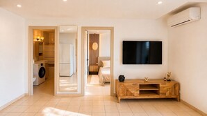 A modern living room with a flat-screen TV, a wooden console, and a laundry area with a washing machine and dryer. - T2 Marina di Fiori - Mountain view for 2 people (Porto-Vecchio)