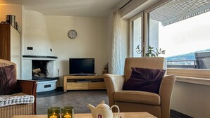 Olohuone, jossa on takka, televisio, sohva, pöytä, jonka päällä on kirja, teekannu ja kynttilöitä.