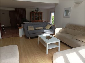 A living room with a grey sofa, beige sofa, and a white coffee table. There is a wooden cabinet with glass doors and a plant.