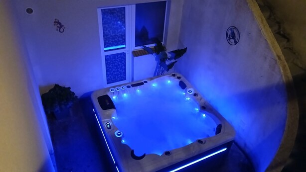 A hot tub with blue LED lights, a window with a star-patterned curtain, and a logo on the wall. - Ideal for groups: spa and leisure villas (Guégon)