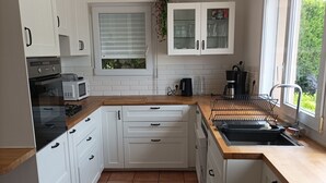 A modern kitchen with white cabinets, a wooden countertop, a built-in oven, a microwave, a sink, and a window with a view of greenery. - Ideal for groups: spa and leisure villas (Guégon)