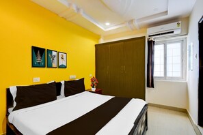 A hotel room with a bed, a window with curtains, a wall-mounted air conditioner, and three framed pictures. - Deluxesri Vinayaka Luxury Rooms (Hyderabad)
