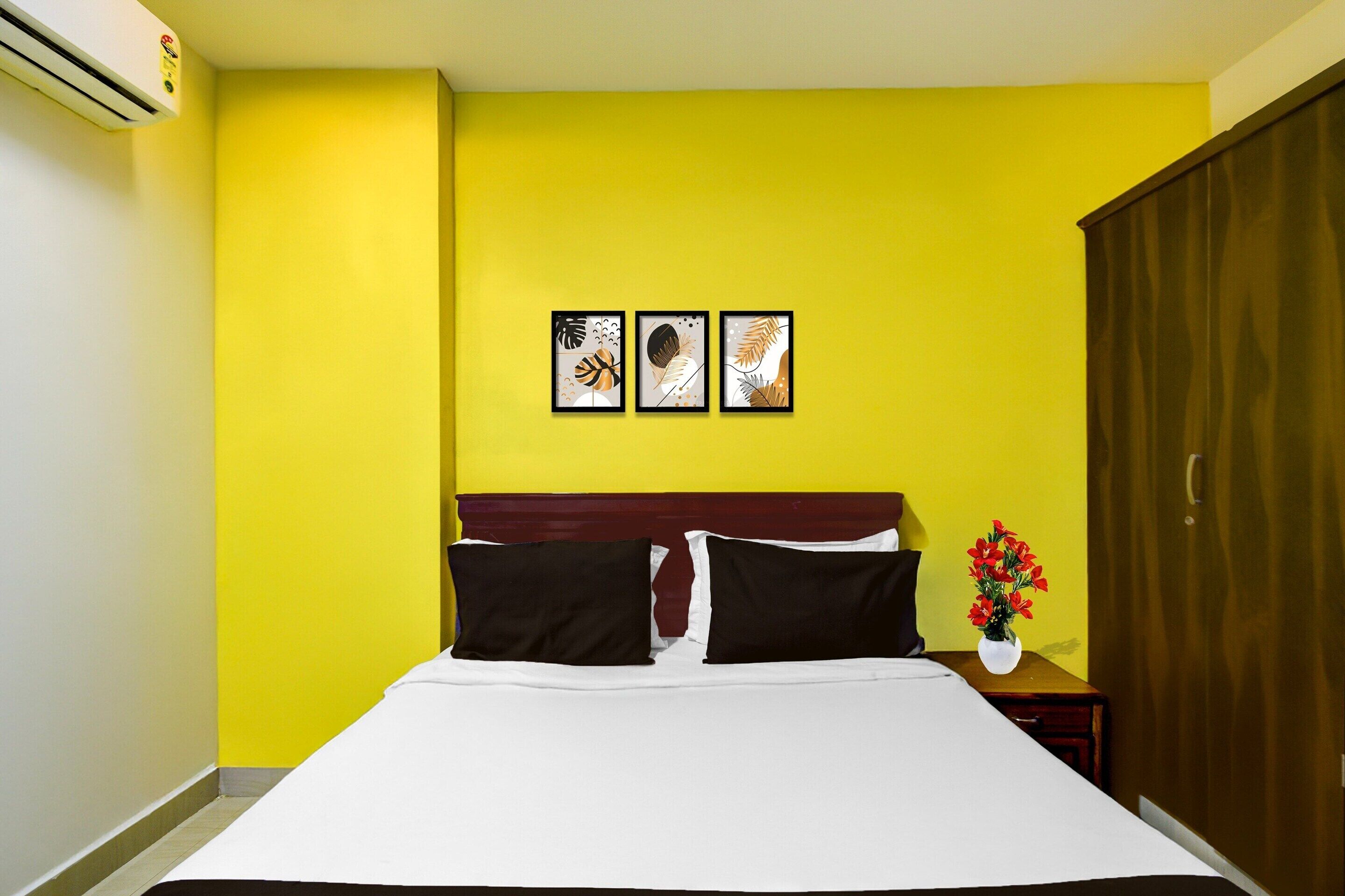 A bed with white sheets, two black pillows, and a wooden headboard. There are three framed artworks on the wall above the bed.
