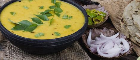 A bowl of soup garnished with herbs, accompanied by sliced onions and a lime wedge on a rustic wooden surface.