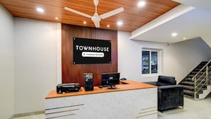 Een receptiebalie met een bord waarop 'TOWNHOUSE Company-Serviced' staat, een plafondventilator en een trap.