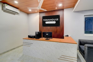 A reception desk with a sign reading 'TOWNHOUSE Company Serviced,' a ceiling fan, and a window with blinds. - Deluxemiyapur Metro Station (Hyderabad)