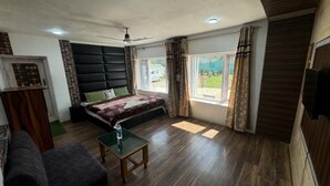 Una habitación con cama, una mesita, un ventilador de techo y una ventana con cortinas.