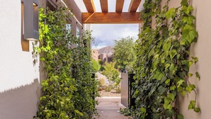 Ein schmaler Pfad, gesäumt von üppigem Grün, der zu einem Gebäudeeingang mit einer hölzernen Pergola darüber führt.