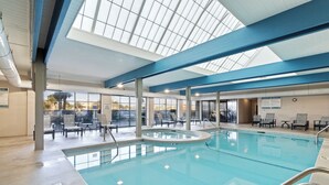 Ein Hallenbad mit klaren Glasdecken, Liegestühlen und Blick ins Freie.