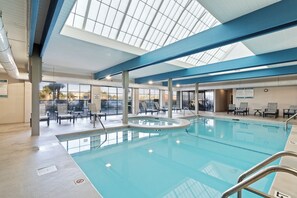 An indoor swimming pool with clear glass ceilings, lounge chairs, and a view of the outdoors. - Bluewater 1205 by Liquid Life (Orange Beach)