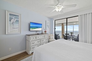 A bedroom with a bed, a dresser, a television, and a balcony with a view. - Bluewater 1205 by Liquid Life (Orange Beach)