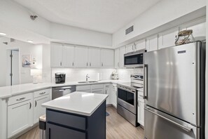 A modern kitchen with white cabinetry, stainless steel appliances, and a central island. - Bluewater 1205 by Liquid Life (Orange Beach)