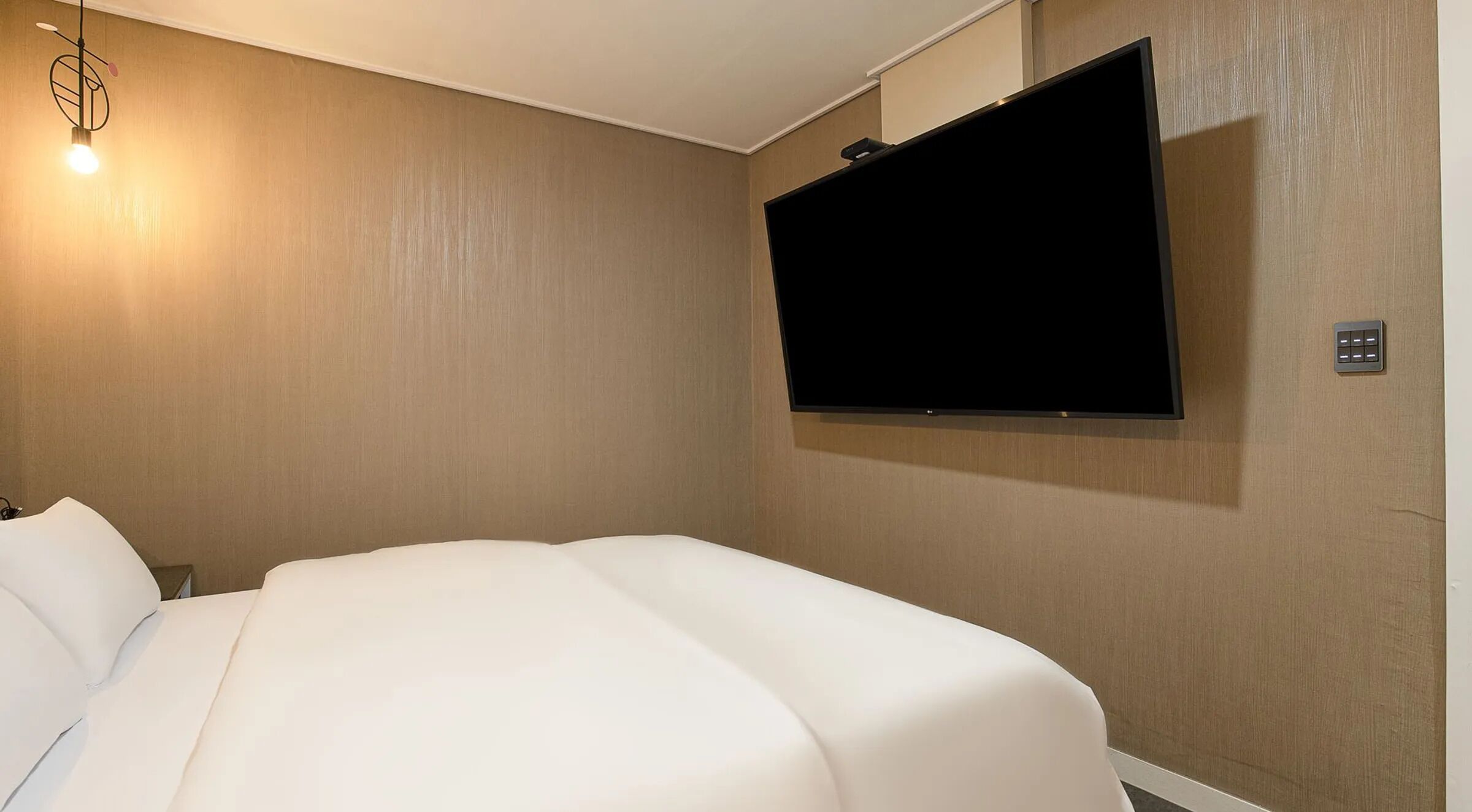 Une chambre d’hôtel avec un lit, un téléviseur fixé au mur et un luminaire.