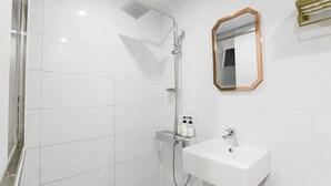 Un bagno con piastrelle bianche, una doccia con soffione manuale, un lavandino con rubinetto e uno specchio con cornice in legno.