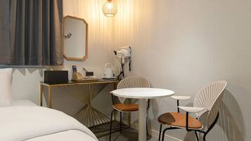A hotel room with a bed, a desk with a lamp, a chair, and a small table.