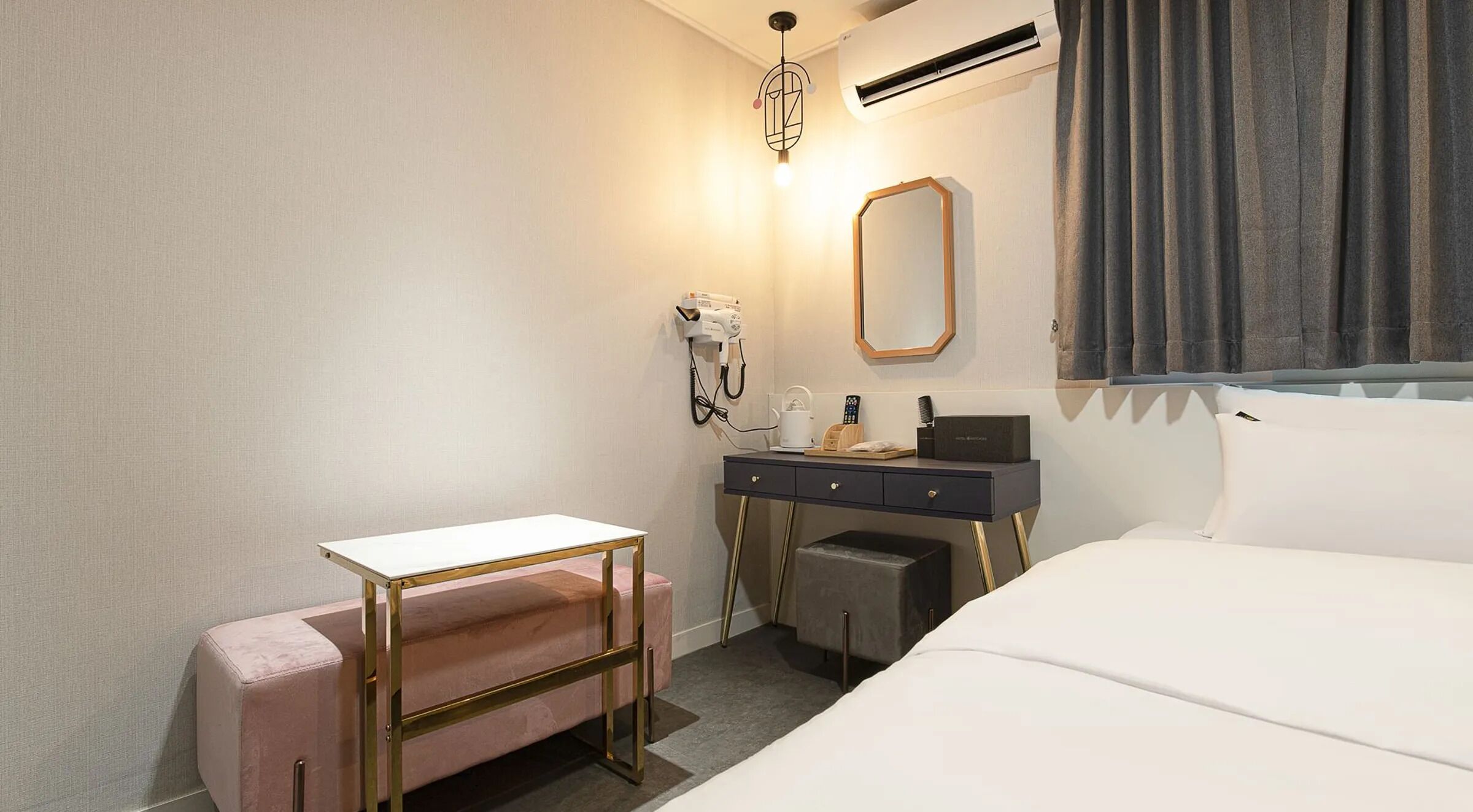 Ein Hotelzimmer mit einem Bett, einem Schreibtisch mit Stuhl, einem Schminktisch mit Spiegel und einer Klimaanlage.