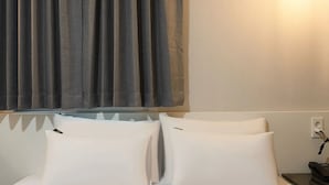 Camera d'albergo con un letto, cuscini bianchi, una tenda grigia e una presa a muro.