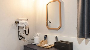 Camera d'albergo con asciugacapelli, specchio, macchina del caffè, telecomando, pettine e scatola di fazzoletti.