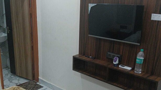 A room with a TV mounted on a wooden panel, a water bottle on the panel, and a bed with a tiger-patterned blanket. - ; THE PERFECT HAVEN FOR YOUR COMFORT'' A PEASEFUL RETREAT , (Vrindavan)