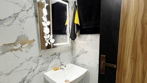 A bathroom with a marble wall, a white sink, a mirror, and a black door. - ; THE PERFECT HAVEN FOR YOUR COMFORT'' A PEASEFUL RETREAT , (Vrindavan)