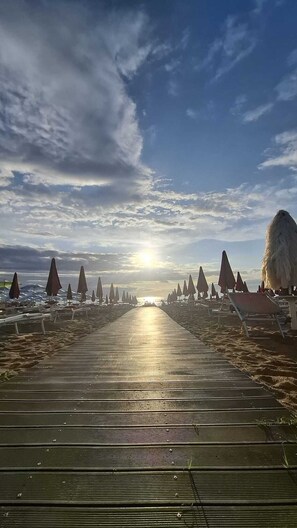A wooden boardwalk leading to beach umbrellas and a thatched structure, under a partly cloudy sky. - Apartment 50m from the beach | 7 guests | terrace & bike path (Martinsicuro)