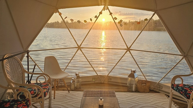 A tented area with a view of a lake at sunset, wicker chairs, and a small table. - Luxe waterfront cottage with a private dome (Whitchurch-Stouffville)