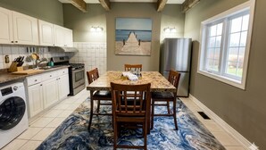 A kitchen with white cabinets, a dining table with chairs, a painting on the wall, and a large window. - Luxe waterfront cottage with a private dome (Whitchurch-Stouffville)