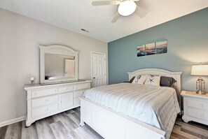 Um quarto com cama, penteadeira, espelho e obras de arte na parede.