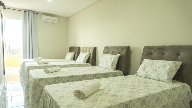 Habitación de hotel con cuatro camas, cada una con cubrecama y almohadas estampadas, una ventana con cortinas y un equipo de aire acondicionado en la pared.