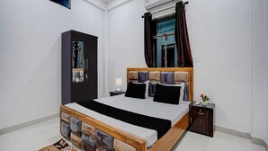 Quarto com cama, guarda-roupa, mesa de cabeceira, cortinas e ar condicionado.