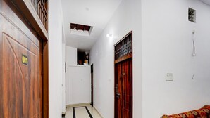 Um corredor com uma porta de madeira identificada como '001', uma porta vermelha e um sofá com capa estampada.