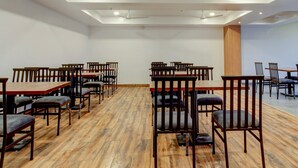 Una habitación amplia con varias mesas y sillas de madera, ventiladores de techo e iluminación empotrada.