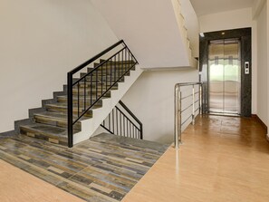 Un escalier avec une rampe en métal, un plancher en bois et une porte d’ascenseur en verre.