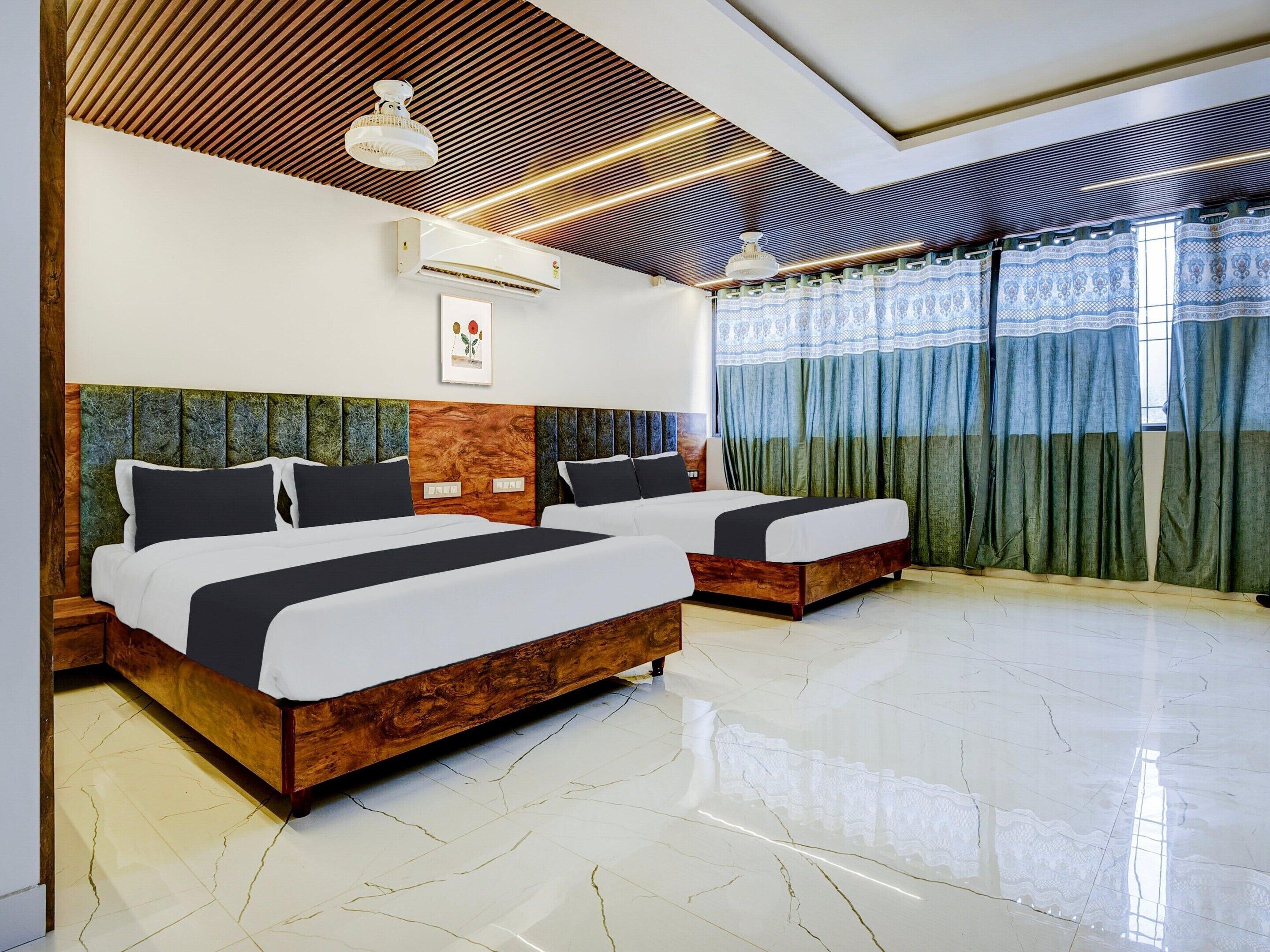 A hotel room with two beds, a wooden headboard, a ceiling fan, an air conditioner, and a window with curtains.
