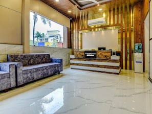 A reception area with a marble floor, a sofa, a reception desk, and a water dispenser. - Super Townhouse Madgaon (Margao)