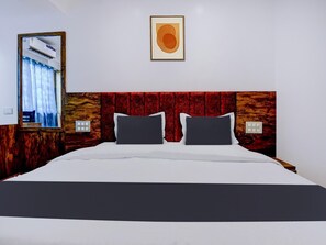 Une chambre d’hôtel avec un lit, un miroir, une fenêtre avec des rideaux, un climatiseur fixé au mur et un tableau encadré.
