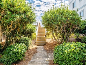 A wooden pathway leading to a building with a staircase. - Observation Cove #217 (Topsail Beach)