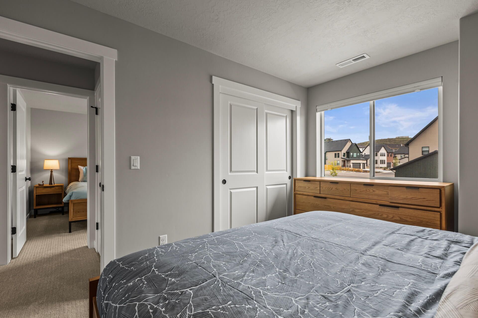 A bedroom with a bed, dresser, and a window with a view of houses.