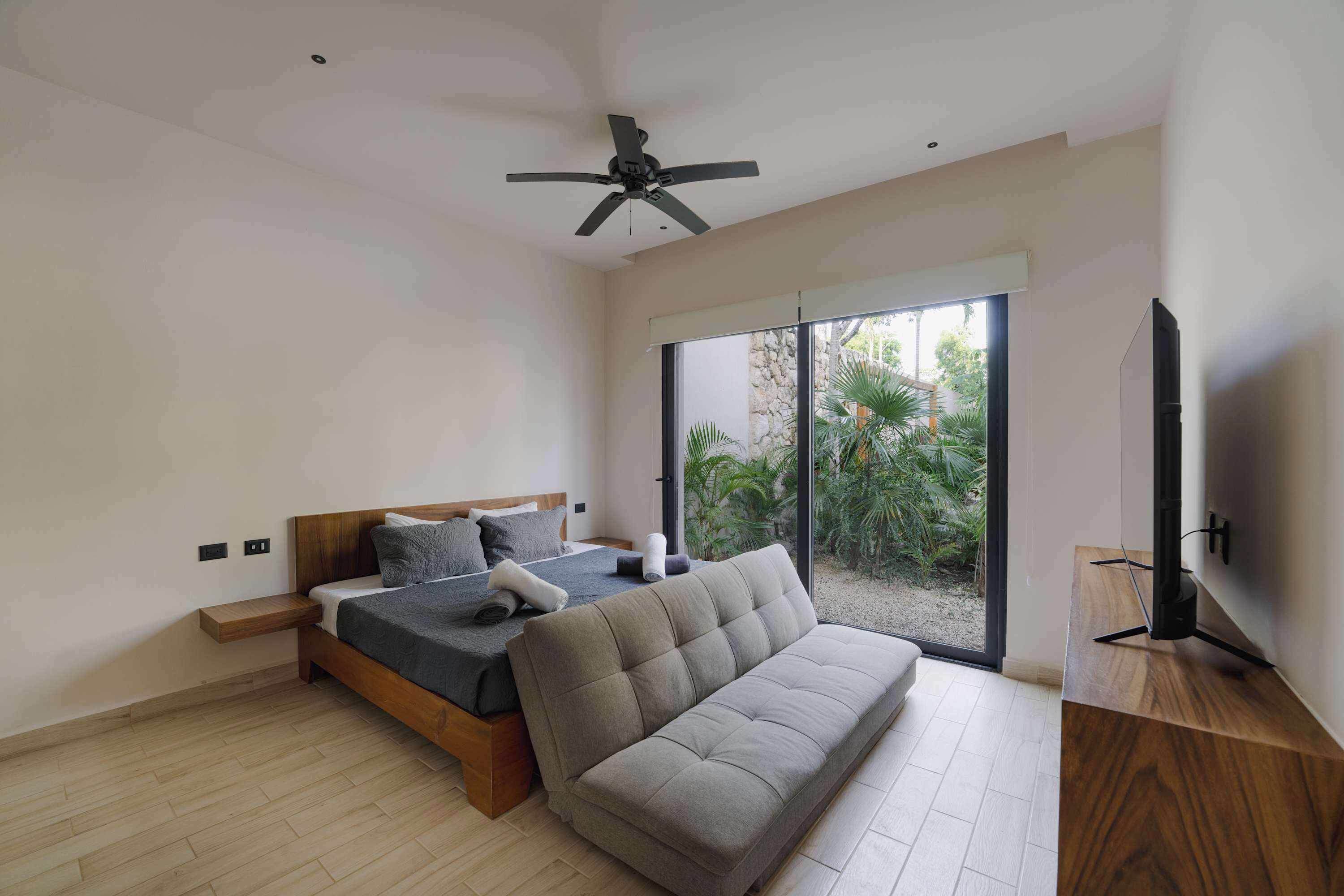 A modern bedroom with a bed, a sofa, a TV, and a ceiling fan.